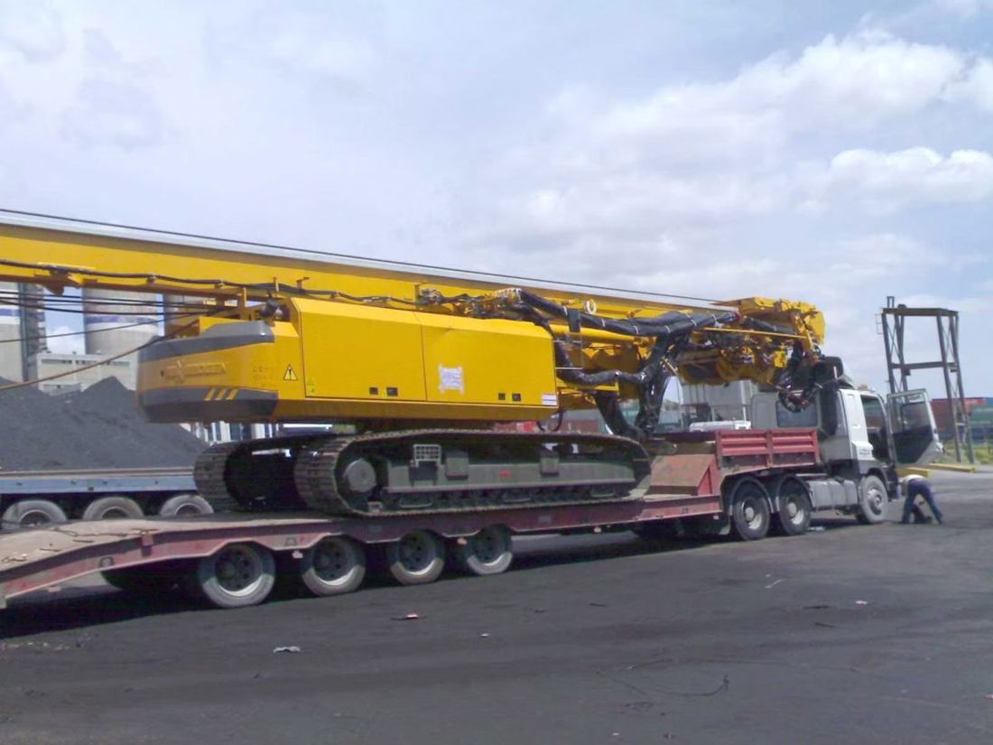 Yellow tracked heavy machine loaded on a low-bed trailer at a port