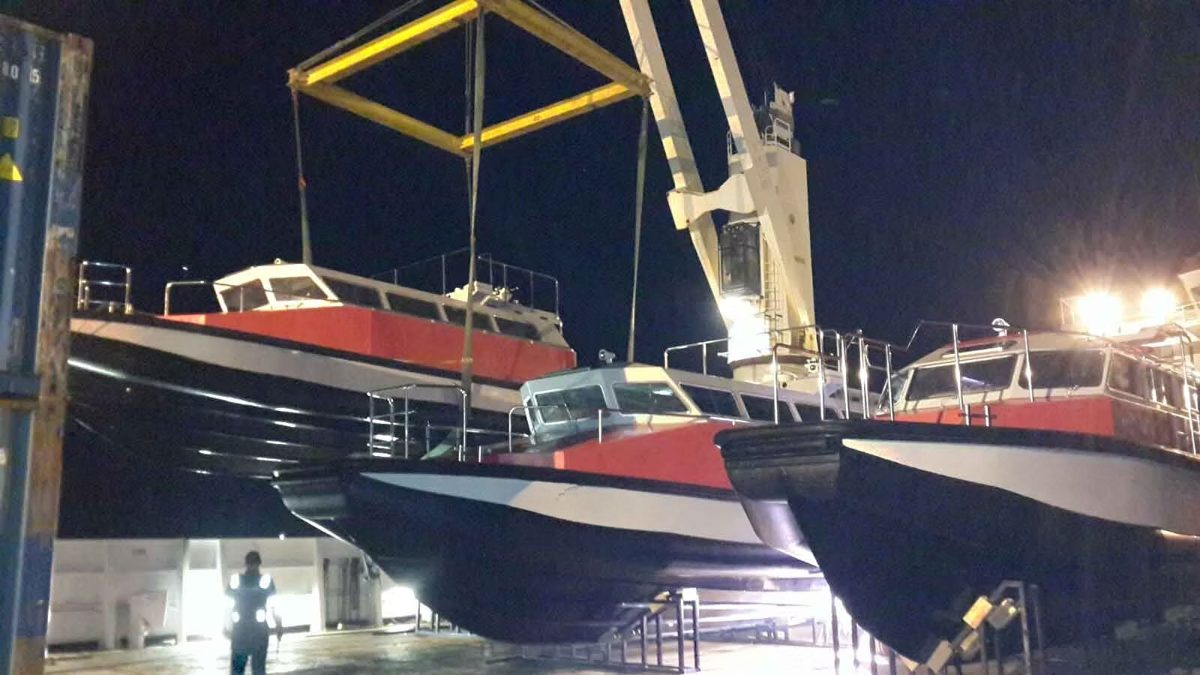 Boats on cradles and a spreader frame under a ship crane at night